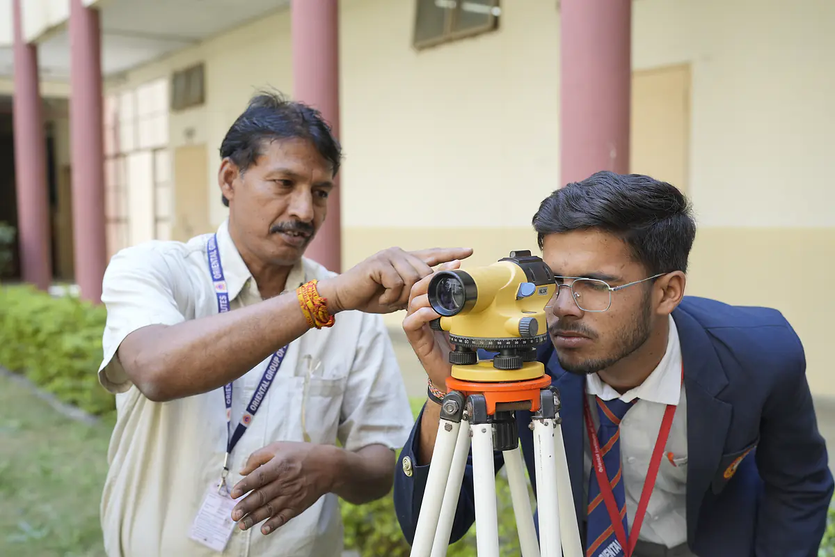 A faculty member guides a student using a surveying level
